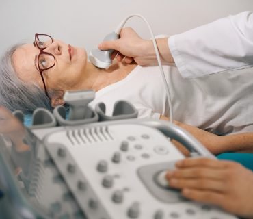 Uzist diagnostician conducts examination of the thyroid gland on ultrasound machine for an elderly lady, the doctor uses modern equipment